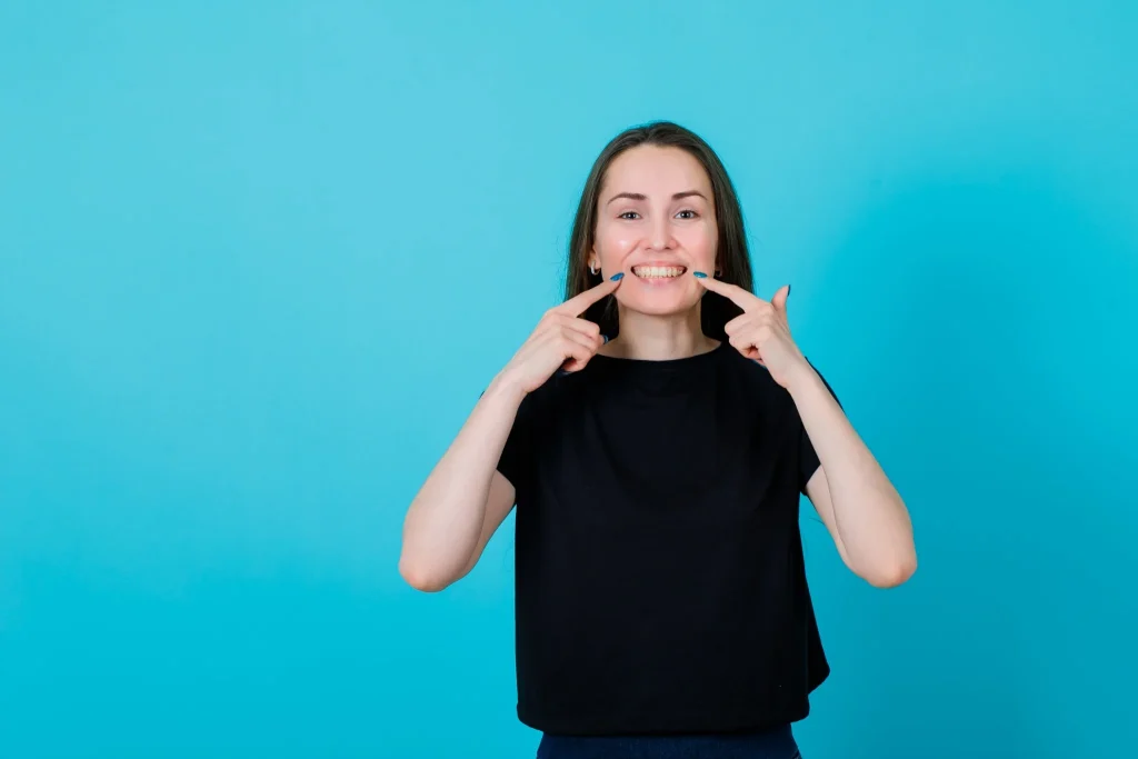 Young woman pointing to her teeth after retainer treatment